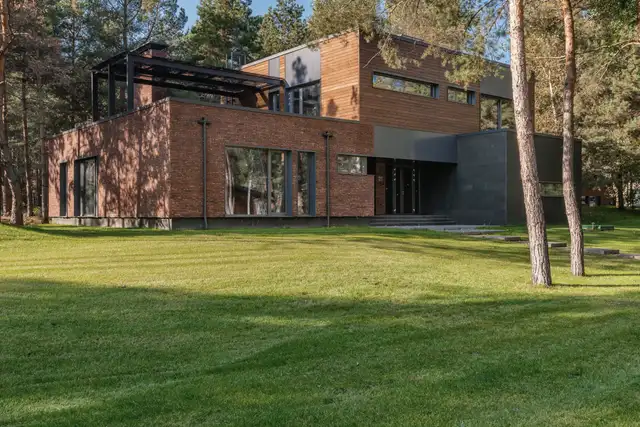Two-storey house in brick and dark panels with a timber-clad upper floor, set on a lawn among pines
