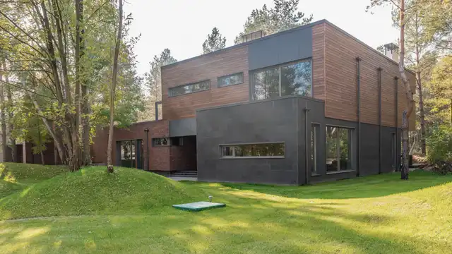 Two-storey house clad in cedar and charcoal panels, set on a sloping lawn below tall firs