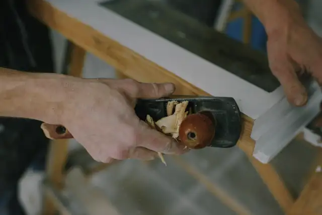 A joiner planing a wooden frame on a workbench, seen from above